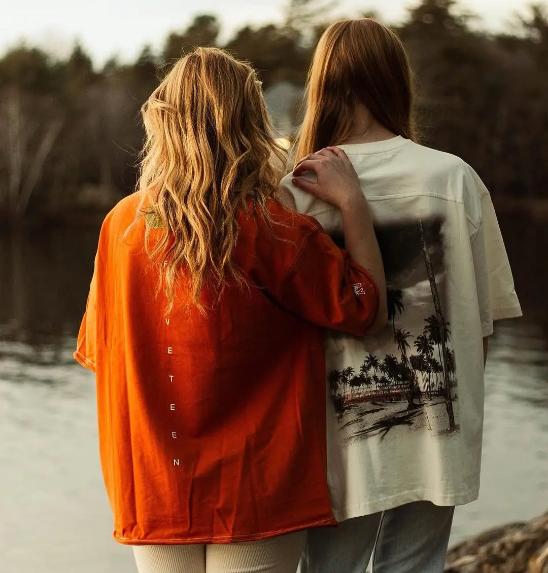 Two friends seen from behind by a lake, one in an orange Sunset overshirt
