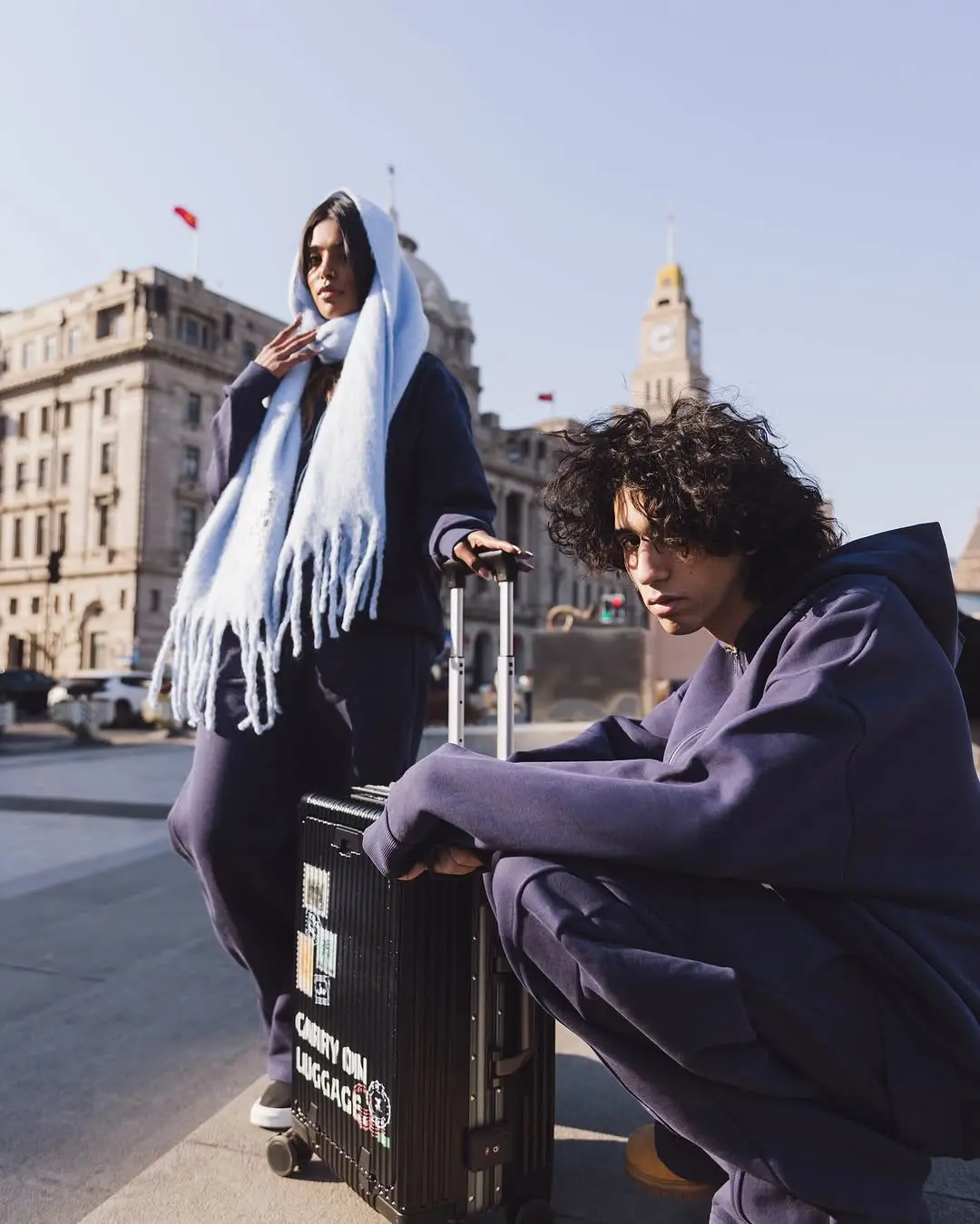 Two models in navy fleece hoodies and a pale blue scarf with a carry-on suitcase in Shanghai