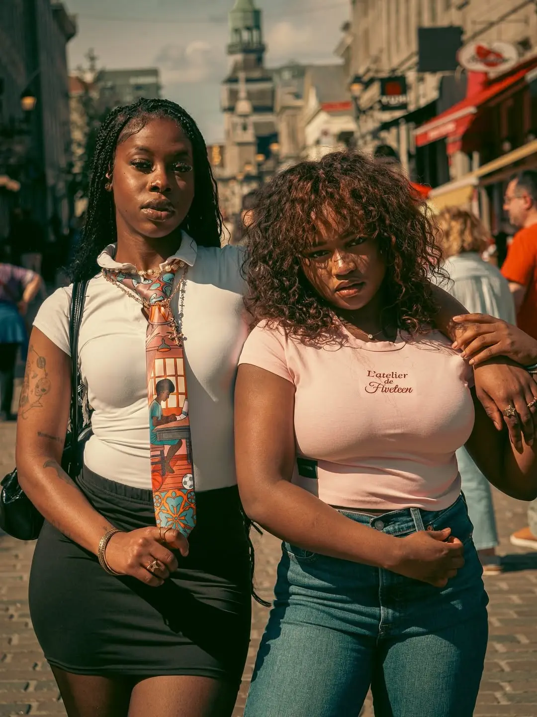 Two women on a busy street, one in a pale pink L’atelier baby tee