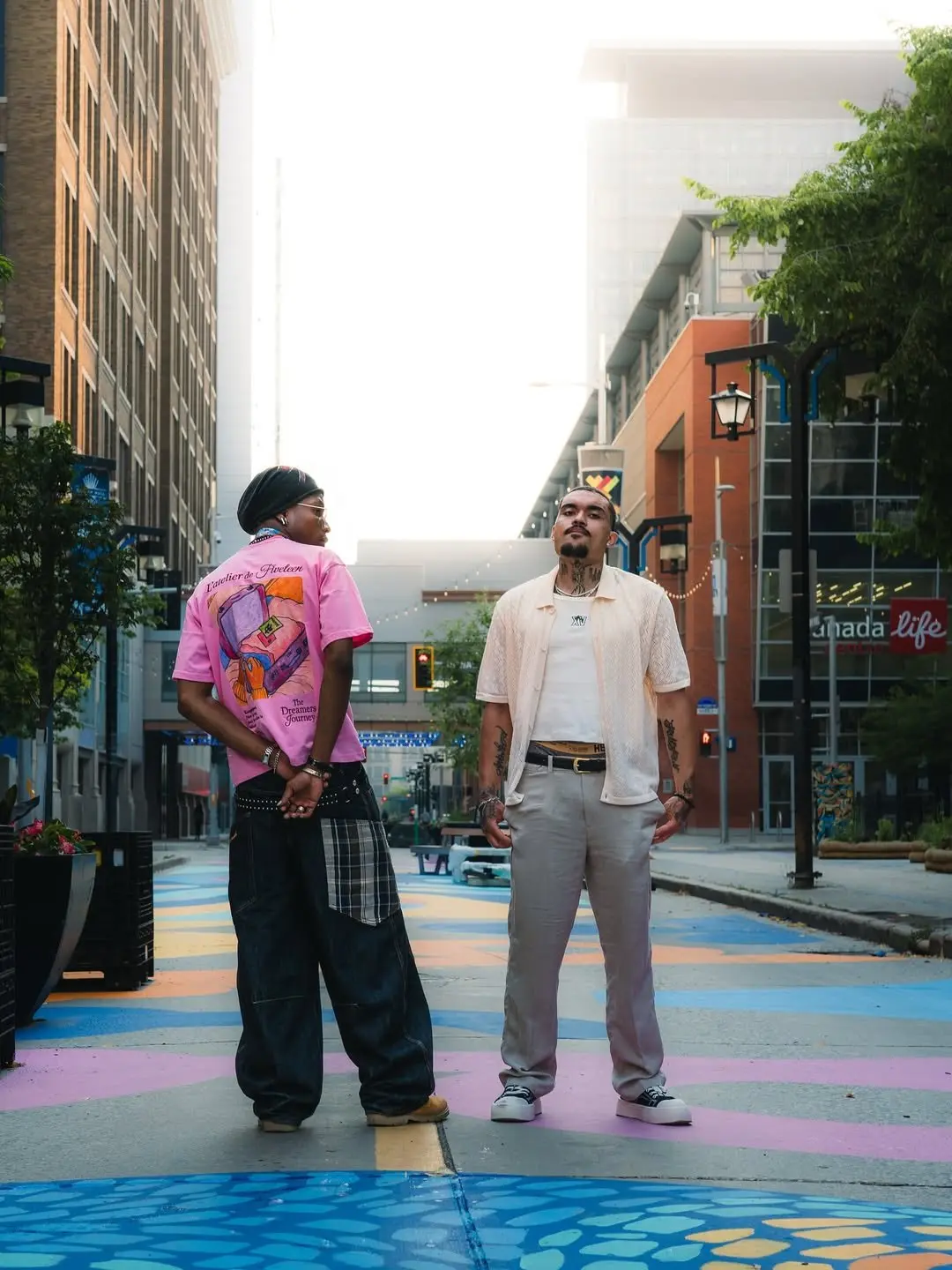 Two men on a painted street, one in an oversized pink graphic tee