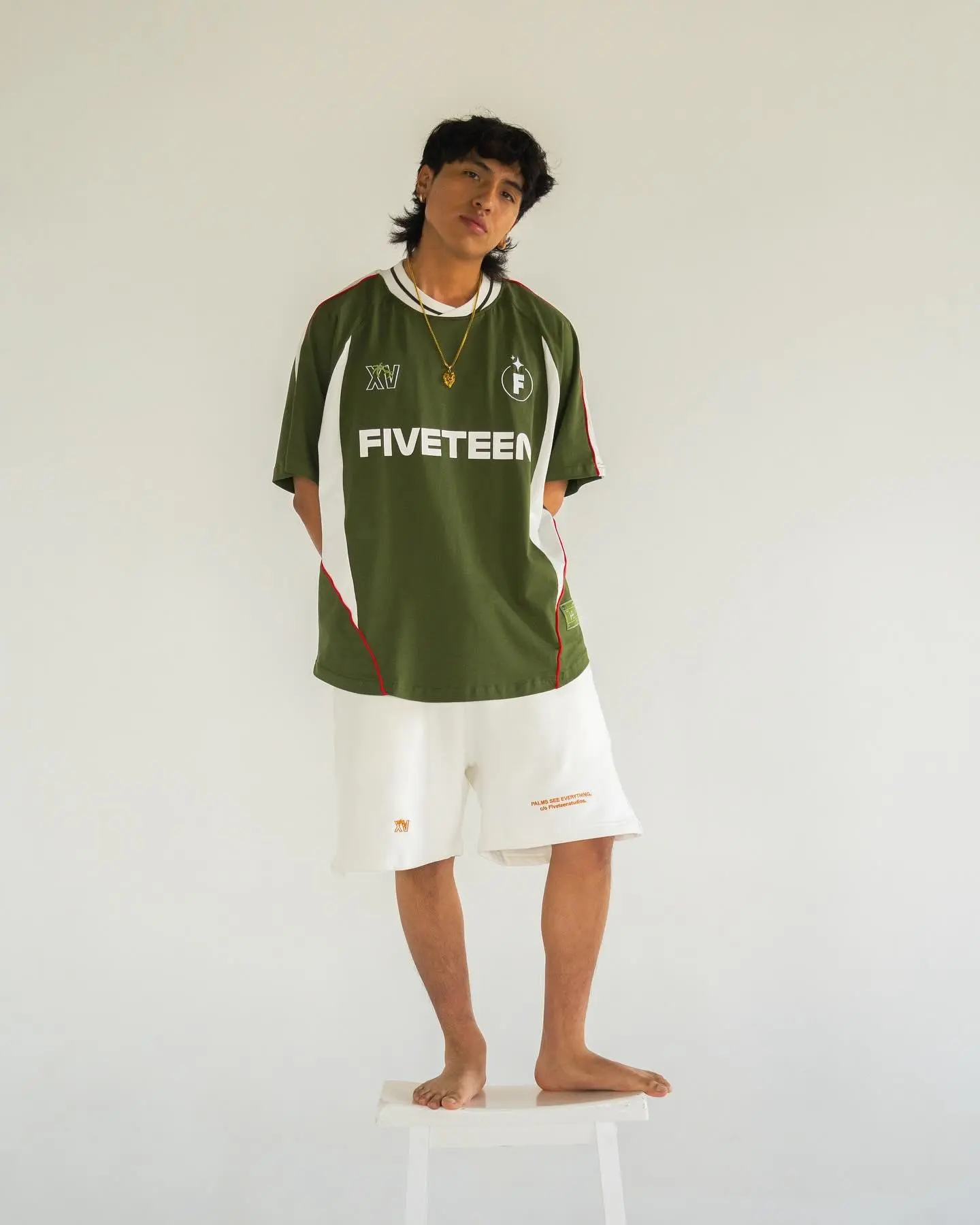 Model standing on a stool in a green Fiveteen football jersey and white shorts