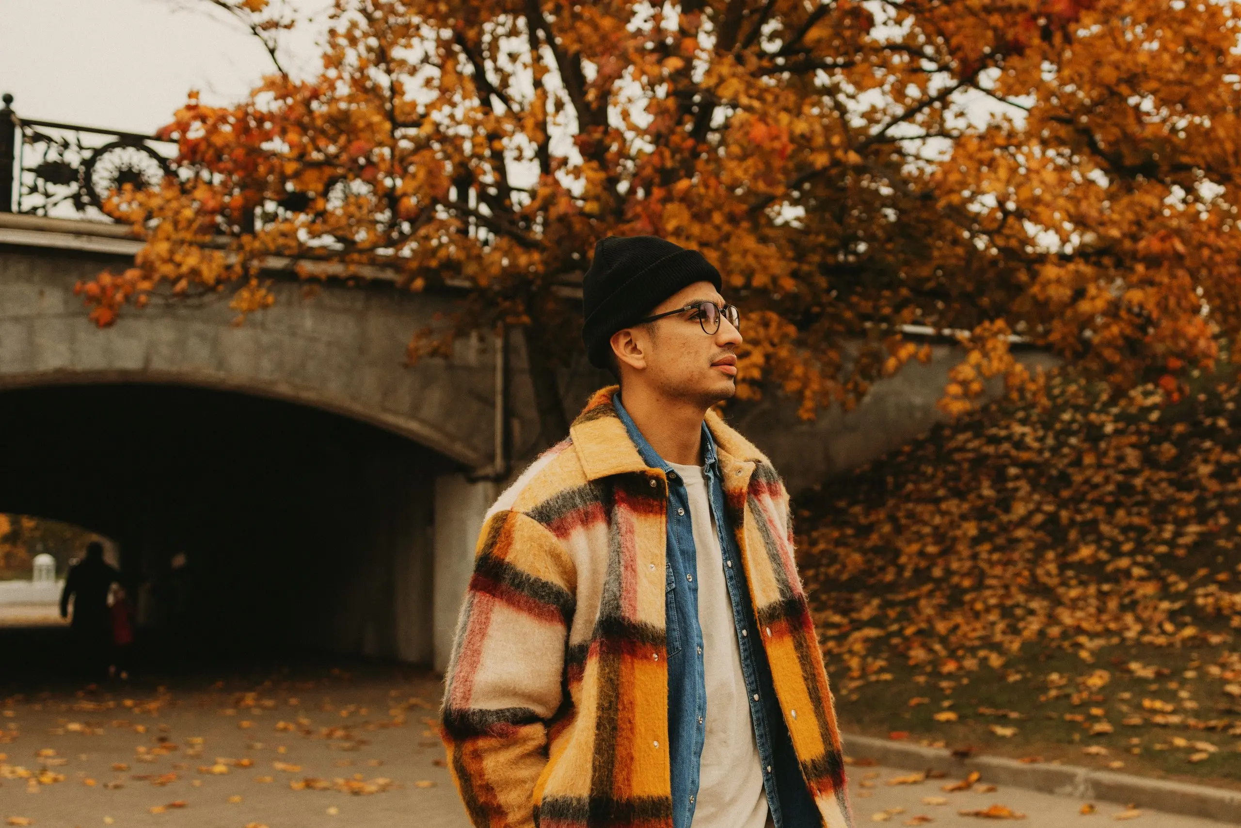 Plaid wool overshirt over a denim shirt and black beanie on a man by an autumn bridge underpass