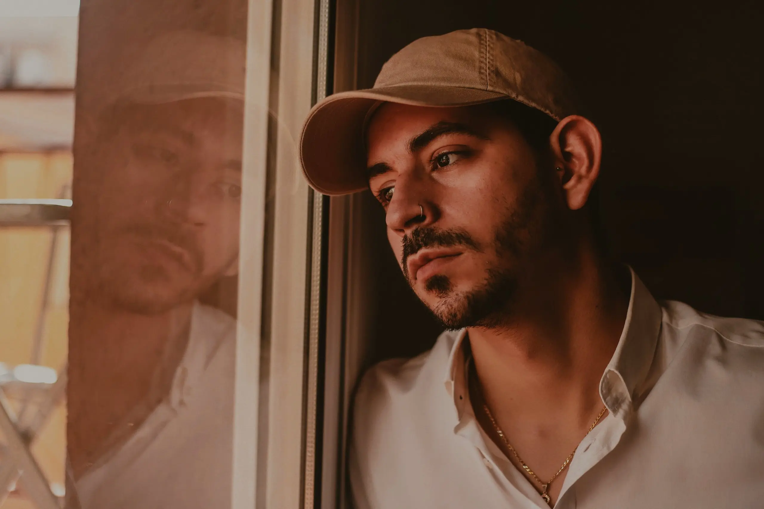 Stone cotton cap and white shirt on a man looking out of a window in soft, warm light
