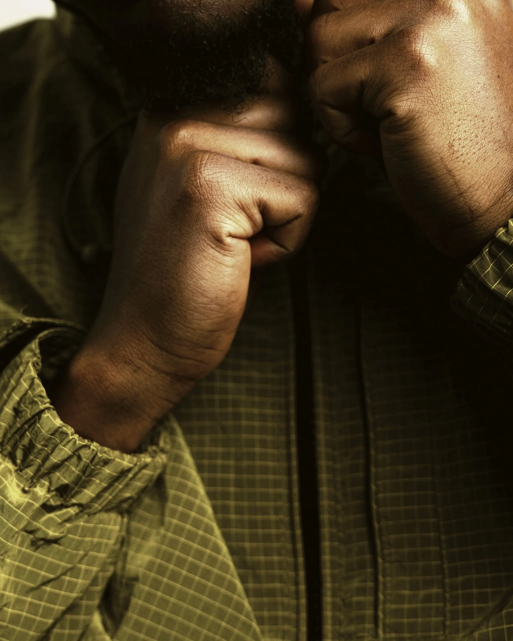 Olive ripstop jacket in close-up, hands pulling up the collar, face out of frame, warm side light
