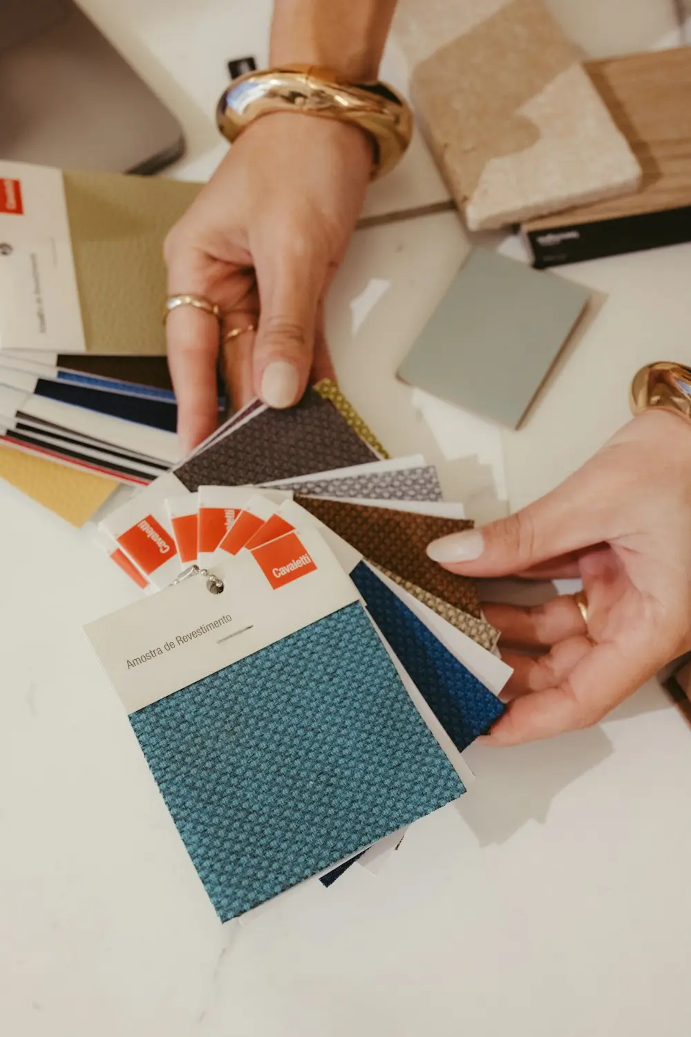 Hands choosing between fabric swatches spread across a table