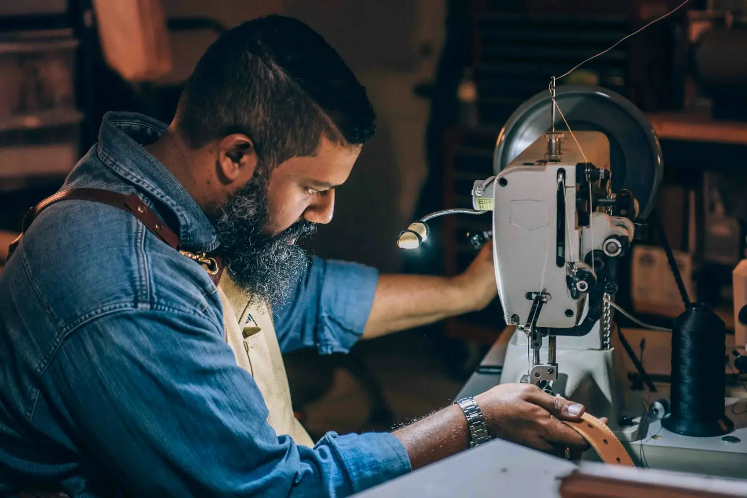 A leatherworker stitching at a sewing machine in a dim workshop